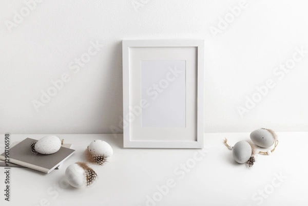 Fototapeta Frame mockup with decorative easter eggs in natural colours and notepad on the white table. Happy Easter concept, copy space for your text.