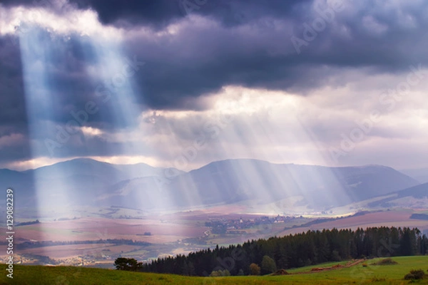 Fototapeta Sunlight beams over clouds in mountains. Rays in cloudy sky