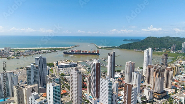 Fototapeta Cargo ship maneuvering in front of the large and modern city of Itajaí, with its grand skyscrapers.
