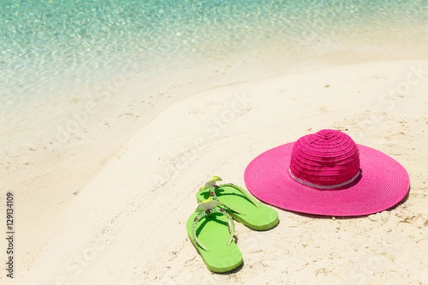 Fototapeta Pink beach hat and green slippers in the golden sand by sea shor