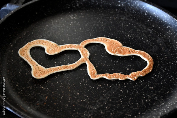 Fototapeta A pancake in the form of two joined hearts on a black spotted pan. selective focus. Maslenitsa holiday. curly pancakes