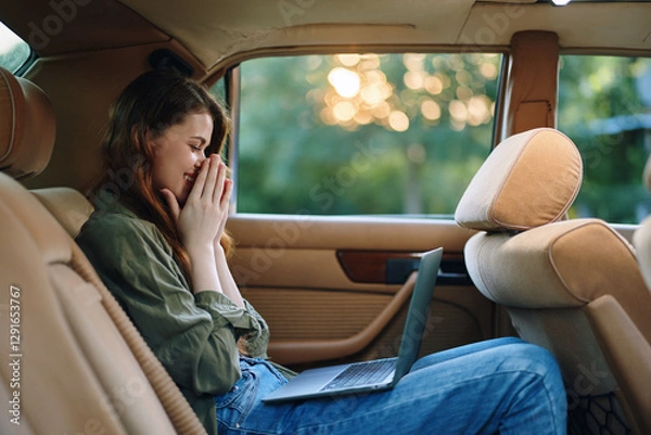 Fototapeta A stressed young woman in casual attire sitting in the backseat of a car, working on a laptop, surrounded by green nature during sunset, reflecting on challenges.