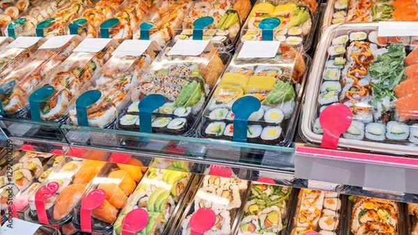 Fototapeta Sushi in a refrigerated display case in a sushi store, a variety of rolls, nigiri and sashimi with fresh salmon, avocado, shrimp and other ingredients, Japanese cuisine, perfect for takeaway or on-the
