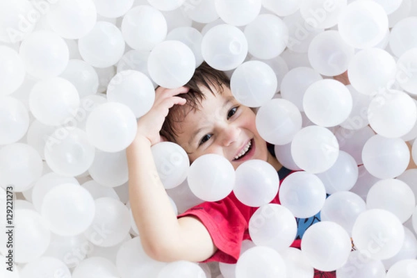 Fototapeta boy hiding under white balls at the playground