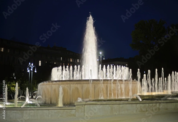 Fototapeta Piazza Castello big round fountain in front of Castello Sforzesco (Sforza Castle) in Milan, Italy, in the evening with dark blue sky. Selective focus