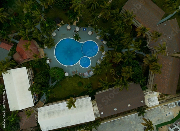Obraz A pool is surrounded by palm trees and buildings