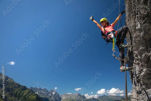 Fototapeta Pretty, female climber on a via ferrata - climbing on a rock in Swiss Alps