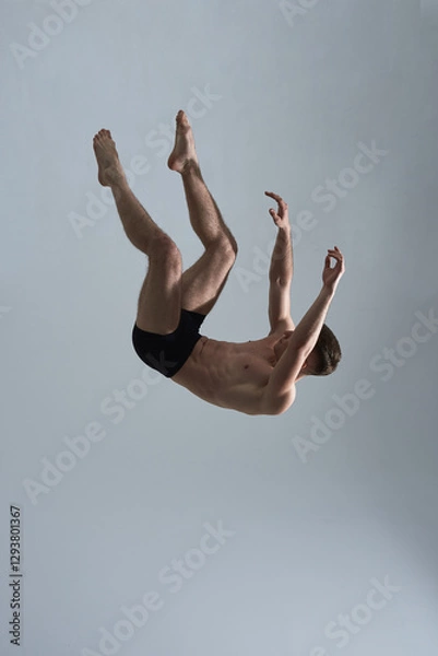 Obraz A male dancer in black shorts is captured mid-air in a falling motion, isolated on a light background, showcasing strength, movement, and artistry.