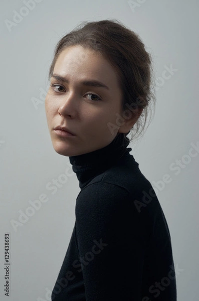 Fototapeta Dramatic portrait of a young beautiful girl with freckles in a black turtleneck on white background in studio