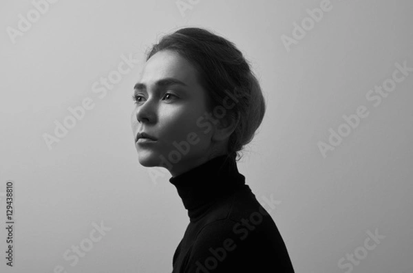 Fototapeta Dramatic black and white portrait of young beautiful girl with freckles in a black turtleneck on white background in studio