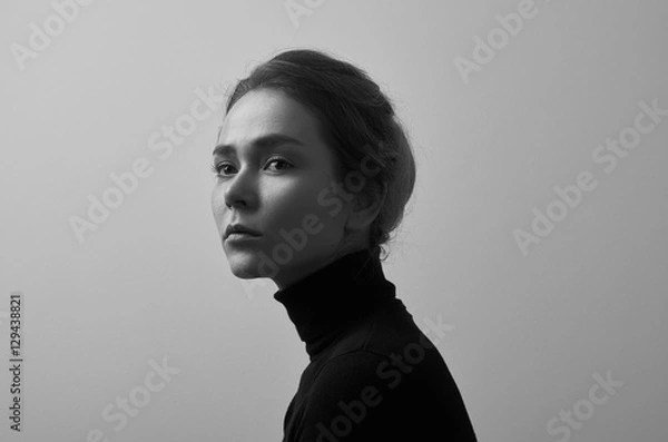Fototapeta Dramatic black and white portrait of young beautiful girl with freckles in a black turtleneck on white background in studio
