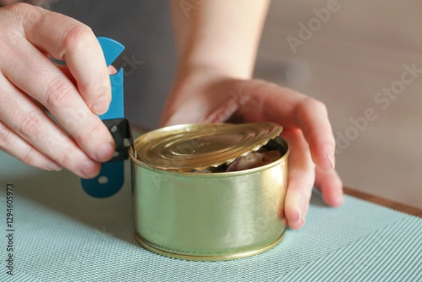 Fototapeta Womans hands open tin can with an can opener. Canned food and special knife