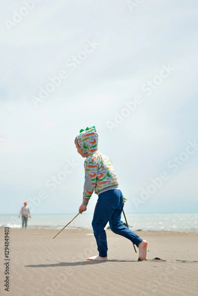 Fototapeta Happy child walking with stick and sand on sea beach in the sun