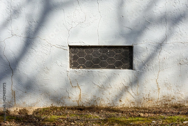 Fototapeta Rectangular crawl space vent, ventilation opening with a metal mesh cover. White aging stucco wall, surrounded by cracks and weathering