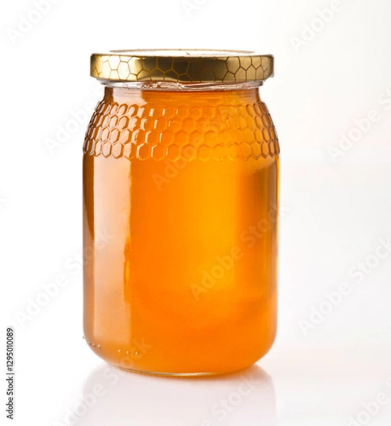 Fototapeta Freshly harvested honey in a clear jar with a golden lid on a white background