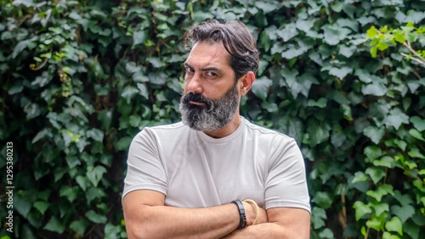 Obraz A middle-aged, fair-skinned, bearded man looking at the camera with an angry expression in a close-up shot, outdoors in a wooded area