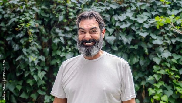 Obraz A middle-aged, dark-haired man with a beard and fair skin making funny facial expressions while looking at the camera in a close-up shot in a wooded outdoor setting