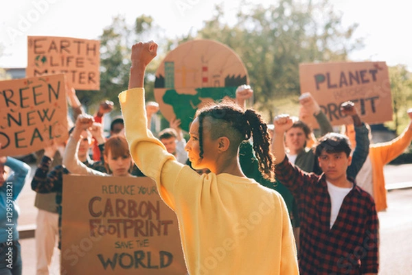 Fototapeta Young activists protesting for climate change action - Group of diverse young activists at a climate protest holding signs and raising fists in support of environmental causes