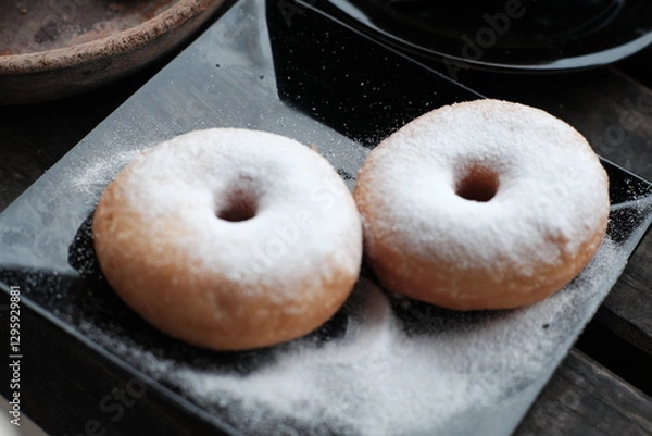Obraz Fresh donuts sprinkled with powdered sugar, perfect for breakfast or a sweet snack.