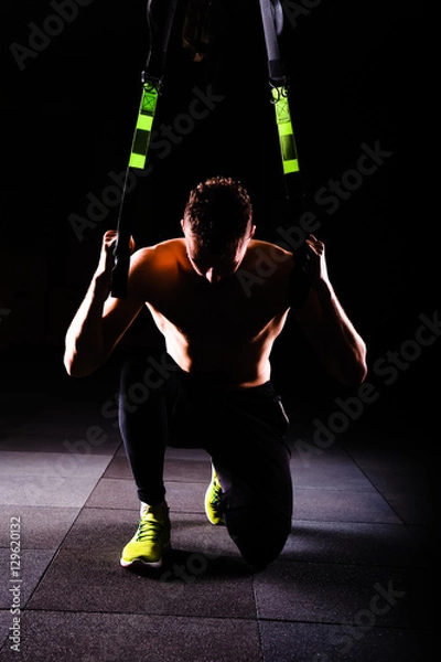 Obraz One young handsome brave curly bearded muscled man with a beard makes Total Resistance eXercises fitness trx straps working out in gym crossfit