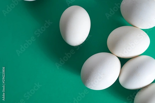 Fototapeta Overhead view of white eggs on a vibrant green background.