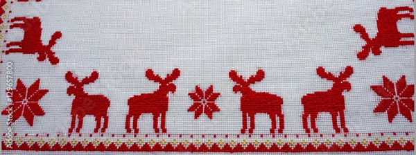 Fototapeta Cross-Stitched red deer on the white tablecloth. Christmas background
