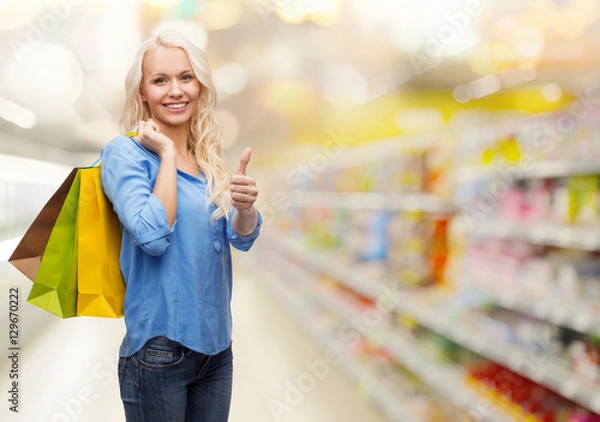 Obraz smiling woman with shopping bags showing thumbs up