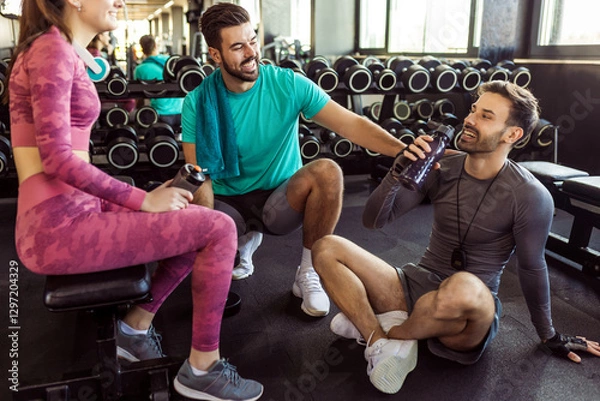 Fototapeta Three people rest at the gym. They talk, drink water and rest between training.