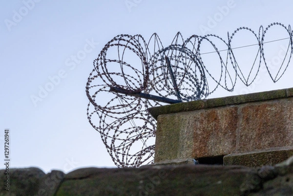 Fototapeta Concrete wall with barbed wire, view from below against the sky. The top edge of fence. Scotland