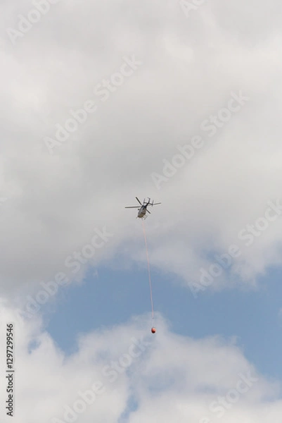 Fototapeta Fire fighting helicopter with trailing a water bucket on the way back to a bushfire