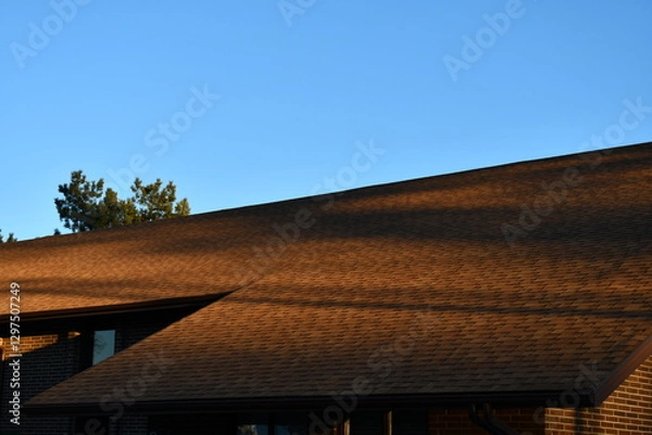 Obraz Long shadows cast over large brown shingled roof.