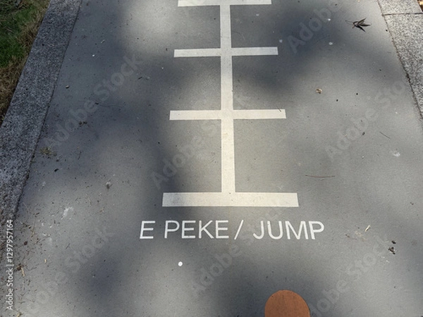 Fototapeta Markings on the tarmac of a playground have the words 'E Pike' and 'Jump'. Maori and English Language.New Zealand