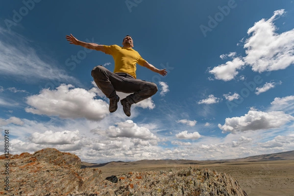 Fototapeta A man in bright clothes jumps into the air and freezes in a cheerful pose with a view of the sky. Funny pose while jumping with open arms against the background of nature.