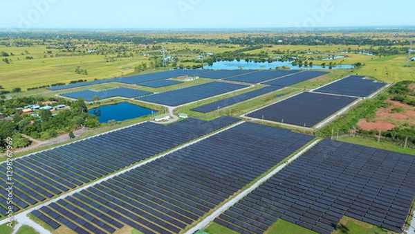 Fototapeta Drone shot aerial view solar energy array provides renewable power in large scale facility surrounded by greenery and water in rural place. Solar farm at the countryside