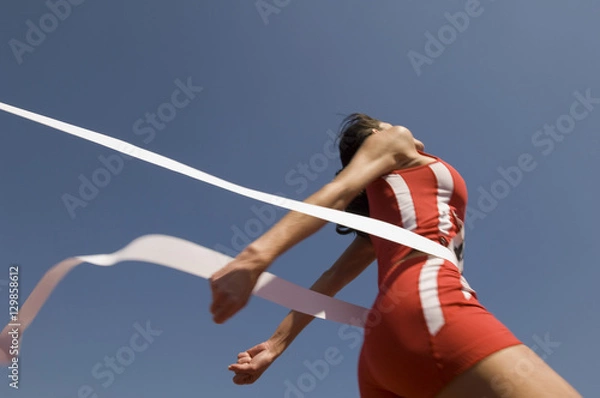 Fototapeta Low angle view of young female athlete crossing finish line against clear blue sky