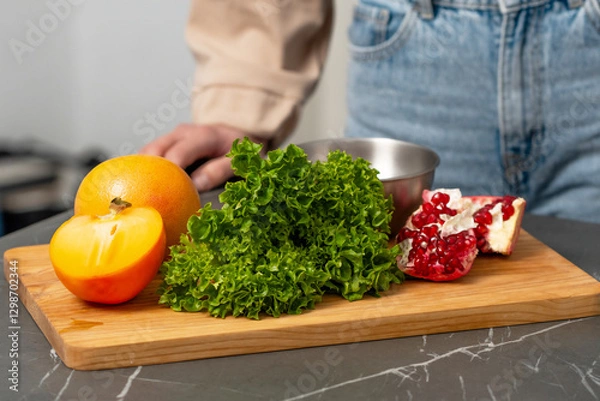 Fototapeta Fresh ingredients on a wooden cutting board showcasing pomegranate, lettuce, and persimmon in a modern kitchen setting