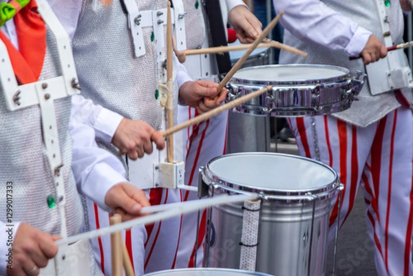 Fototapeta Members of a comparsa play the batucada while advancing in the Tenerife carnival parade, dressed in a white costume with red stripes.