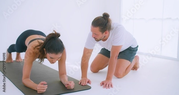 Fototapeta A personal trainer Coaching guides a woman performing push-ups Exercise on a yoga mat in a bright, minimalist studio environment.