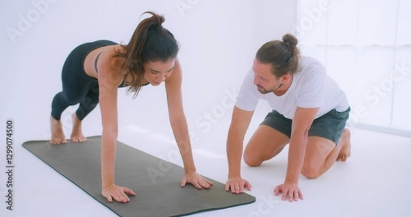 Fototapeta A personal trainer Coaching guides a woman performing push-ups Exercise on a yoga mat in a bright, minimalist studio environment.