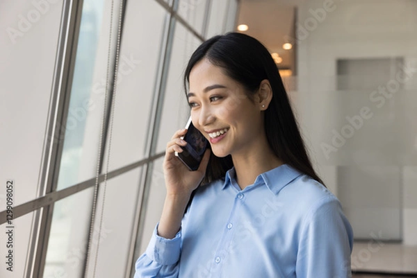 Fototapeta Professional communication. Head shot portrait confident young adult Asian woman manager entrepreneur executive speaking on phone by window in modern office make answer call hold business conversation