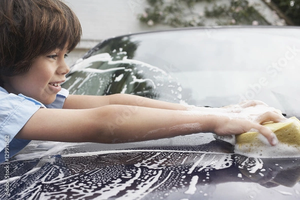 Fototapeta Closeup side view of a young boy washing car with sponge