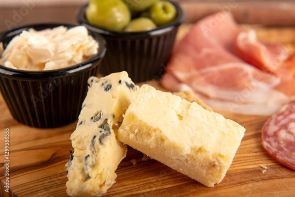 Fototapeta A cheese plate with a variety of cheeses and olives. The cheese is cut into small pieces and arranged on a wooden cutting board