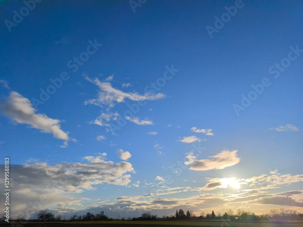 Fototapeta The sun is low over the fields and meadows - the first sunset glow appears in the clouds
