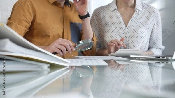 Fototapeta Two accountants conducting a financial audit in their office, closely examining documents with a magnifying glass and calculator. Taxes, audit in business