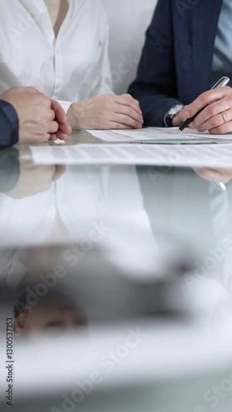 Fototapeta Unrecognizable business people are reviewing contract terms during a meeting while sitting at the glass table in office, vertical close up view. Copy space area