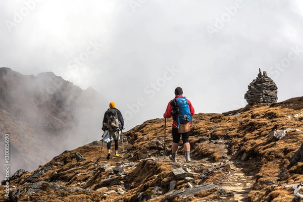 Fototapeta Two Hikers walking on Mountain Slope towards stone Towers