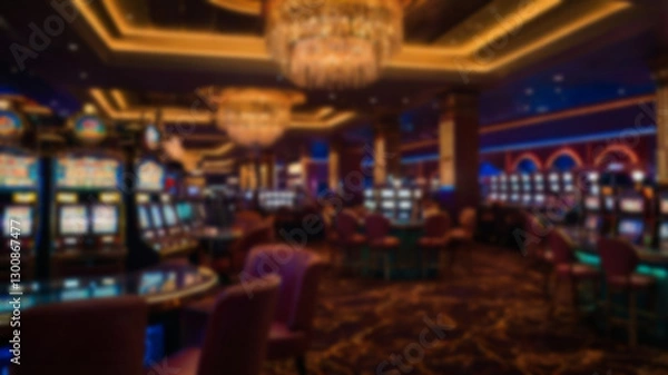 Fototapeta A blurry image of a luxurious casino interior with rows of tables and slot machines, creating an exciting and glamorous atmosphere for entertainment.