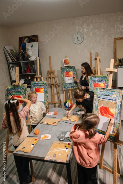Fototapeta Art lesson. School children drawing brush landscapes on easel. Education, creativity and learning concept. Teacher explains to kids how to draw pictures in art class. Childs enjoy painting in workshop