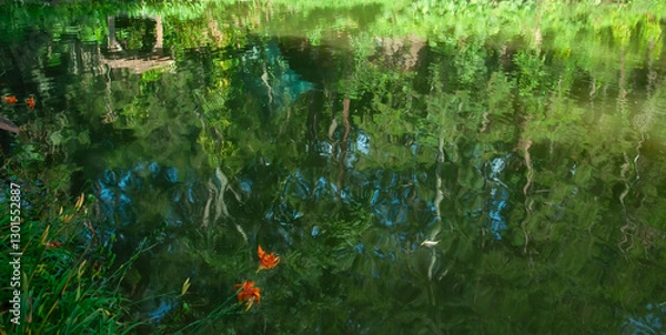Fototapeta distorted reflected vegetation in still water surface of lake with orange colored flowers in foreground
