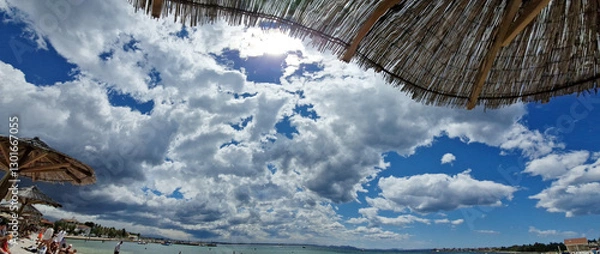 Obraz Sunny beach day with dramatic clouds and straw parasols